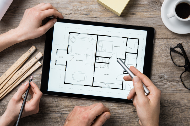 Team of architects working on the house project on a wooden table. Top view of hands pointing architectural project on digital tablet. Interior designer hand working with digital tablet.